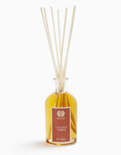 Load image into Gallery viewer, A reed diffuser bottle filled with golden amber liquid, featuring a rectangular reddish-brown label with gold lettering and five light natural reed sticks extending upward, set against a plain white background.