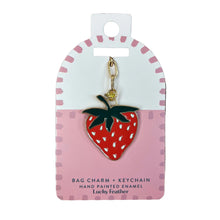 Load image into Gallery viewer, A strawberry-shaped bag charm keychain displayed on its pink and white retail card. The keychain features a red enamel strawberry with white dots, green leaves, and a gold-tone metal ring and chain.