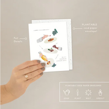 Load image into Gallery viewer, Hand holding a plantable seed paper envelope and card with illustrations on a beige background