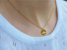 Load image into Gallery viewer, A close-up of a person wearing a delicate gold chain necklace with a small round gold pendant featuring three daisies, styled with a white knit top.