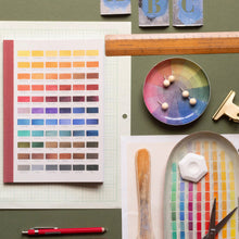 Load image into Gallery viewer, Color swatch book, paint palette, and art supplies on a green surface
