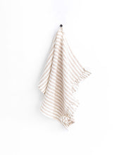 Load image into Gallery viewer, magic linen tea towel with ruffle edge along the short side in neutral stripe, hanging from the attached ribbon loop on a hook on a wall.