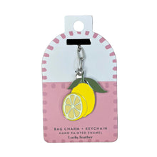 Load image into Gallery viewer, A lemon-shaped bag charm keychain by Lucky Feather, hand-painted enamel, displayed on its pink and white retail packaging card. 
