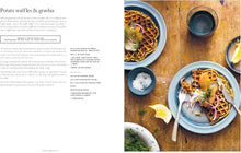 Load image into Gallery viewer, A two-column book spread featuring a recipe for potato waffles &amp; gravlax on the left and a styled food photograph on the right. The photo shows plated golden-brown waffles topped with salmon, greens, and lemon, alongside bowls of seasoning and a dark cup on a rustic wooden table.
