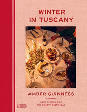 Load image into Gallery viewer, Book cover for 'Winter in Tuscany' by Amber Guinness, featuring a warm-toned photograph of a dinner table in the center against a textured pinkish-beige background with a red vertical band on the left.
