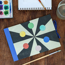 Load image into Gallery viewer, Notebook with geometric design on a wooden surface with art supplies.
