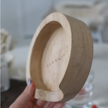 Load image into Gallery viewer, A hand holding a light-colored wooden coaster holder with a smooth, rounded interior and a slightly flared rim, shown against a softly blurred indoor background.
