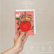 Load image into Gallery viewer, A hand holds a seed paper envelope with a baby card featuring a tomato illustration and the text 'YOU CREATED THE GREATEST HEIRLOOM' against a neutral beige background. White text at the top points to the envelope, and a bottom banner lists product features like soak, plant, wait, and sprout.
