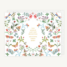 Load image into Gallery viewer, A greeting card with a white background, decorated with a colorful border of illustrated flowers, butterflies, and dragonflies around gold text that reads, 'THE WORLD JUST GOT BRIGHTER! WELCOME SWEET BABY.' A white envelope is partially visible behind the card.
