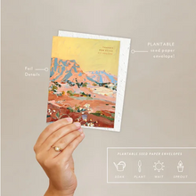 Load image into Gallery viewer, A hand holds a printed seed paper envelope card and greeting card featuring a colorful desert landscape illustration. The card is shown with callout labels pointing to foil details and the plantable seed paper envelope, plus a small feature panel at the bottom about soak, plant, wait, and sprout.
