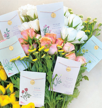 Load image into Gallery viewer, A styled floral arrangement with multiple botanical-themed cards attached to stems, each card featuring a small gold circular pendant on a string. The flowers include white roses, pink roses, yellow daisies, and pale blue flowers, arranged on a light neutral background.
