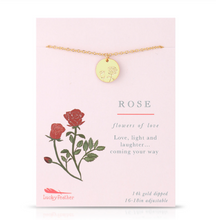 Load image into Gallery viewer, A gold rose-themed necklace with a round engraved disc pendant, displayed on a light pink card. The card features a red rose illustration and the Lucky Feather brand logo, with text reading 'ROSE' and 'flowers of love'.
