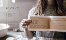 Load image into Gallery viewer, A woman in a gray sweater holds an open vintage-style recipe book, showing handwritten pages. The left side of the image displays a table of contents printed in black text on a light background.
