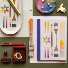 Load image into Gallery viewer, Art supplies including brushes, a color wheel, and printed notebook on a green surface.
