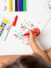 Load image into Gallery viewer, Child's hand holding a red marker over a drawing of ice cream cones with colorful sprinkles on a white surface.
