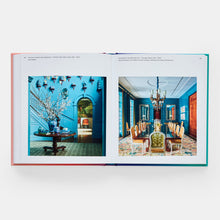 Load image into Gallery viewer, An open hardcover book showing two interior design photographs on the spread, photographed against a clean white background.
