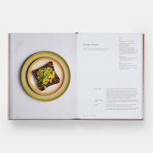 Load image into Gallery viewer, An open cookbook spread showing a recipe page with a photo of a plated food dish on the left and recipe text on the right, photographed against a light gray background.
