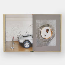 Load image into Gallery viewer, Open book showing two images: a small car model and a plated dish of cod.
