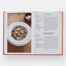 Load image into Gallery viewer, Open cookbook showing a page with a dish of pasta and text on a wooden table.
