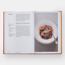 Load image into Gallery viewer, An open cookbook spread showing a recipe for cappelletti with tomato sauce, featuring printed text on the left page and a photo of a bowl of pasta on the right page.
