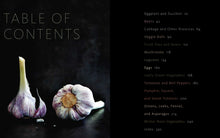 Load image into Gallery viewer, Garlic bulb on a dark surface with a table of contents for a book about vegetables on the right.
